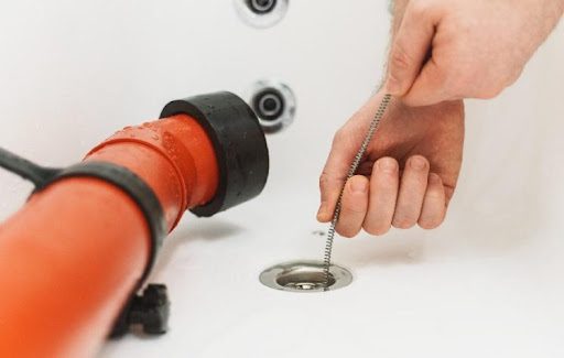 A plumber using a drain auger or drain snake to remove a deep and large clog from a bathroom shower drain in Springfield, MO.