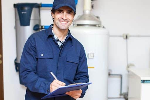 A professional technician in a blue uniform performing a routine check on a residential water heater in Springfield, MO.