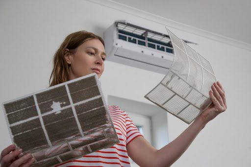 A female homeowner changes her AC’s air filter and compares the dirty filter with the clean one in her home in Springfield, MO.