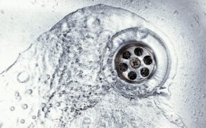 Water flowing into a metal sink drain with visible bubbles.