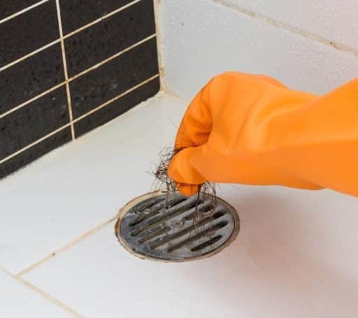 A person in Springfield, MO wearing an orange glove pulling hair out of a floor shower drain that has clogged.