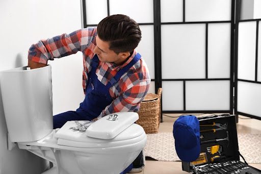 A professional plumber reaching inside the toilet tank to fix the plumbing problem in this home in Springfield, MO.