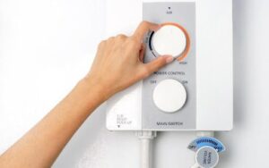 Hand adjusting the temperature knob on a white electric water heater.