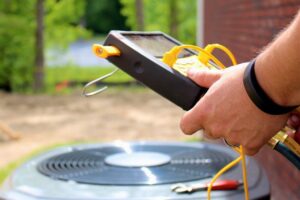 Person using a digital HVAC gauge near an outdoor air conditioning unit, with yellow hoses attached.