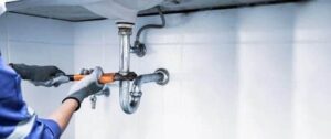 A person wearing gloves uses a wrench to tighten plumbing under a sink.