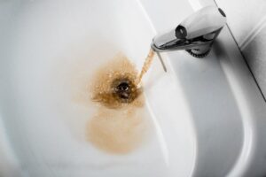 Brown, murky water flows from a faucet into a white sink, indicating possible contamination or plumbing issues.