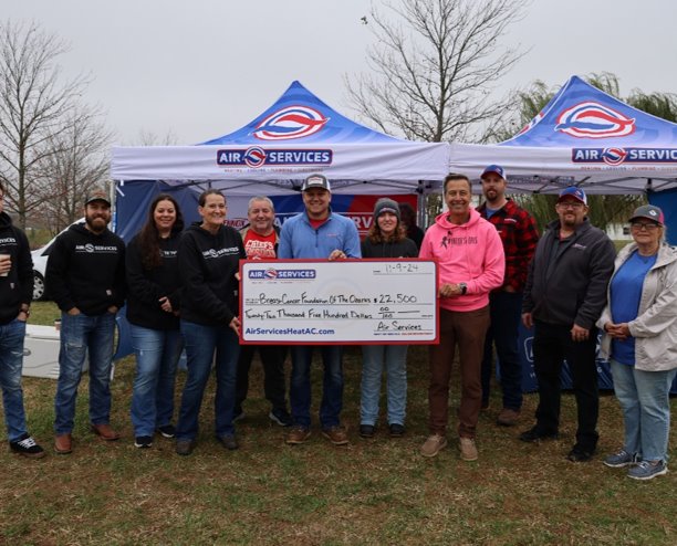 A group of people stand outdoors in front of tents, holding an oversized check for $22,500 made out to a pet charity from Air Services, a company dedicated to improving indoor air quality with electrostatic filters and UV Lights.