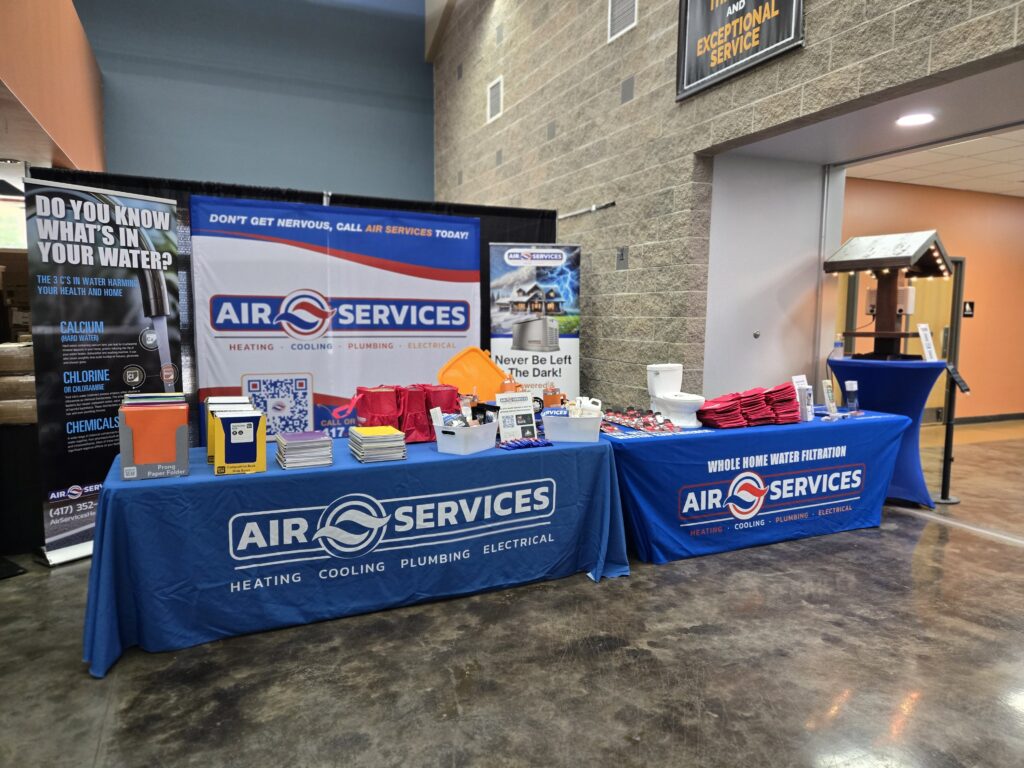 Air Services’ bcfo booth at an indoor event showcases informational banners, promotional items, water testing kits, and branded materials, all neatly arranged on tables against a brick wall.